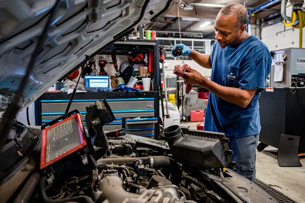 A mechanic checking a component beside an open engine bay