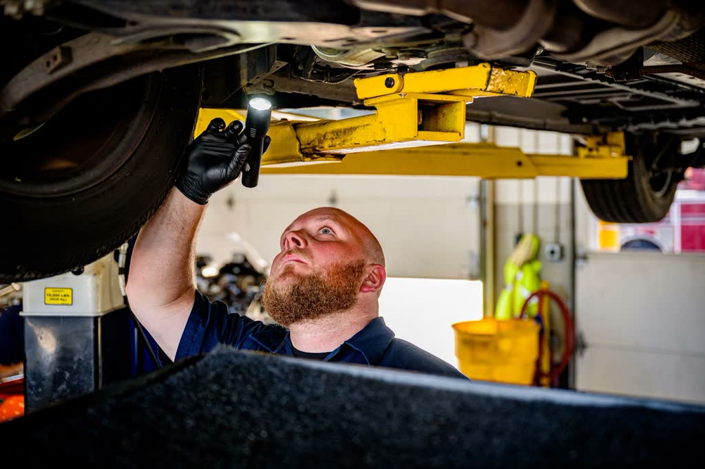 A mechanic inspecting the underside of a car on a lift with a torch