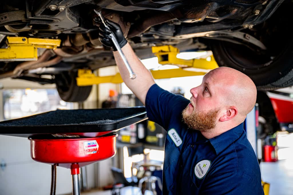 A technician working beneath a car on a lift with an oil drain pan beside him