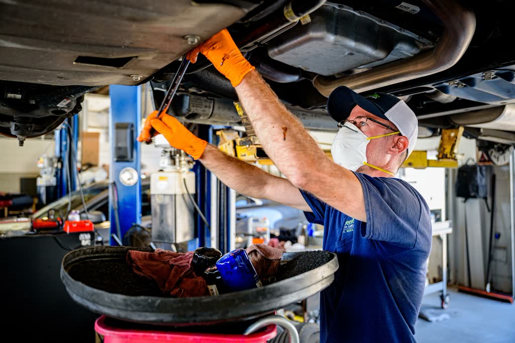 A technician draining engine oil into a catch tray under a car